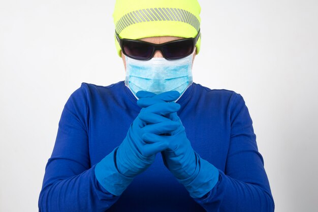 Man in medical mask, sunglasses and protective gloves folded his hands for prayer
