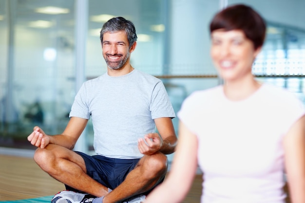 Man meditating in lotus position Smiling man meditating in lotus position with woman in foreground