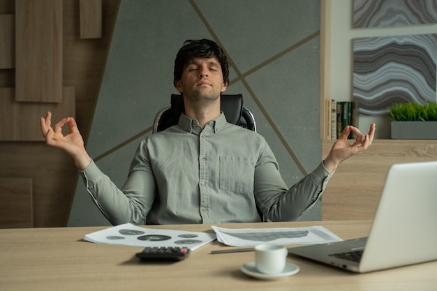 Man meditating in office coping with stress business executive doing yoga at desk in a modern office