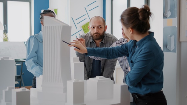 Photo man meeting with women to discuss about building model and to plan project strategy in office. diverse workmates analyzing maquette on table to design layout and construction structure.