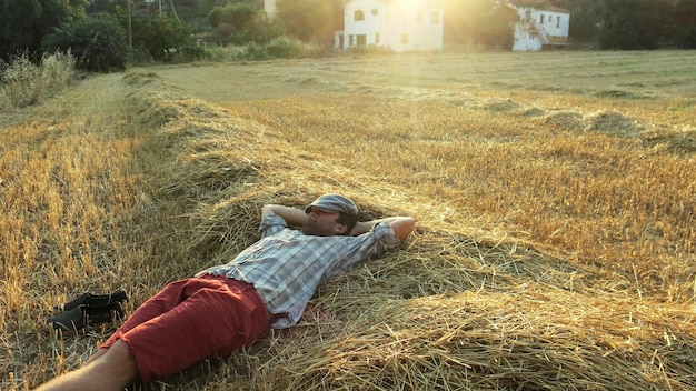 Photo man napping while lying on hay during sunset