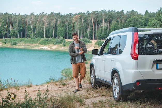 Man near white suv car at the edge looking at lake with blue water