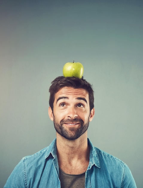 Photo man nutrition and balance apple on head for healthy diet wellness and natural organic food isolated on gray studio background fruit thinking and person with idea for breakfast detox and space