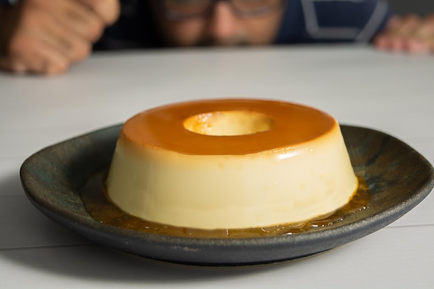 A man observes a pudding or flan on a dark dish