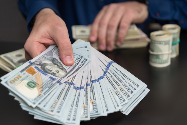 Man offering a bribe or payoff of 100 USD bills holding out a fanned handful across a table in a corruption concept