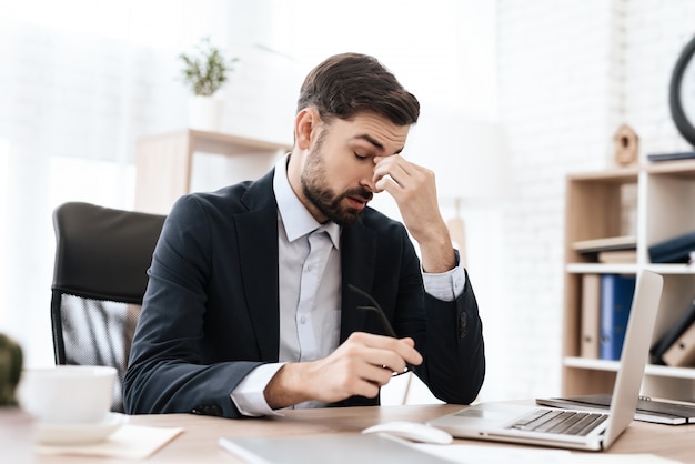 Man in the office is sitting and holding his head in pain.