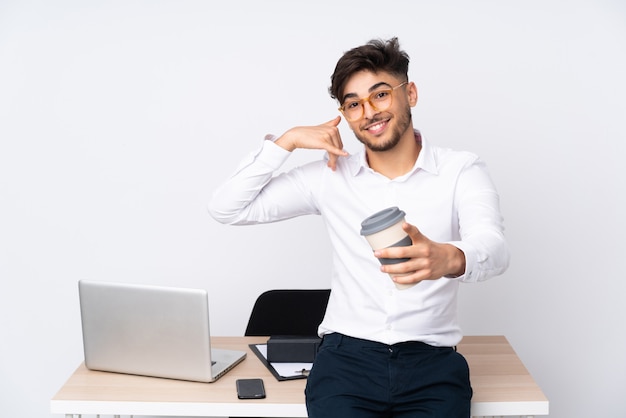 Man in a office isolated on white wall making phone gesture and pointing front