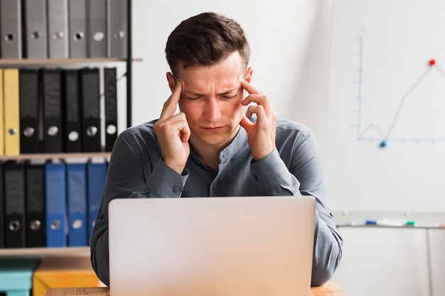 Man in office during pandemic working on laptop and experiencing headache