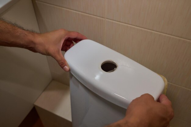 Photo a man opening a toilet tank for the purpose of maintenance or repair tasks at home