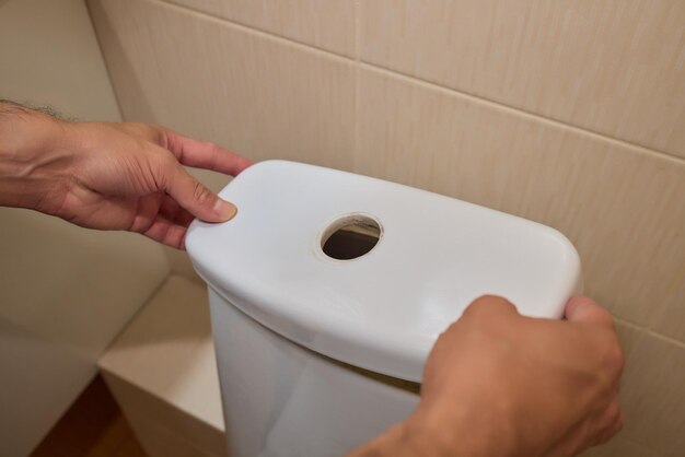 Photo a man opening a toilet tank for the purpose of maintenance or repair tasks at home