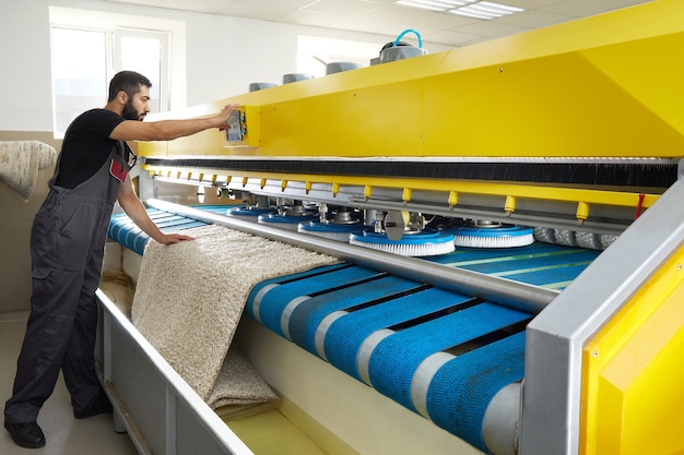 Man operating carpet automatic washing machine in professional laundry service