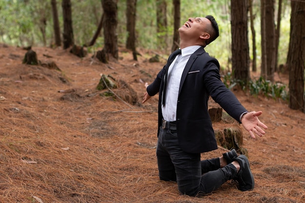 Man in an orange forest kneeling looking at the sky with open arms while laughing.