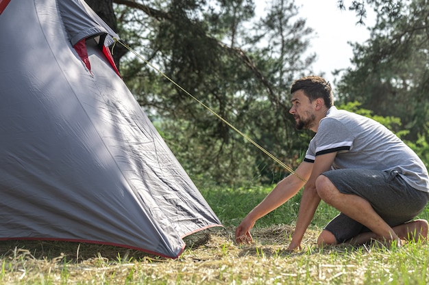 A man outdoors in the process of setting up a tent.