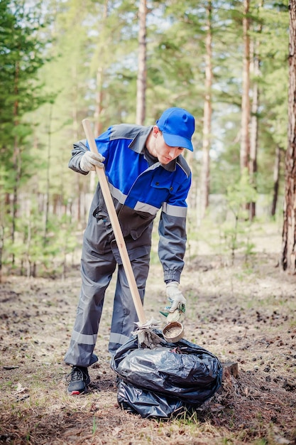 Man in overalls collects garbage and waste in forest Ecological problem of pollution of nature