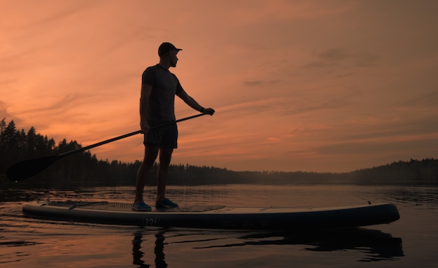 A man on a paddle board at dawn in a picturesque forest lake