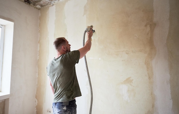 Man painting with airbrush apartment repairment against small window in the daytime