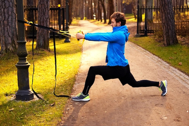 A man in a park improving his legs flexibility with fitness trx strips.