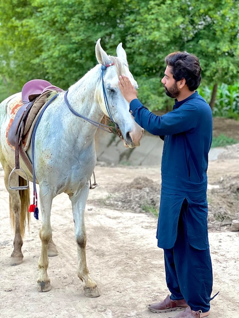 A man petting a white horse on a dirt road.