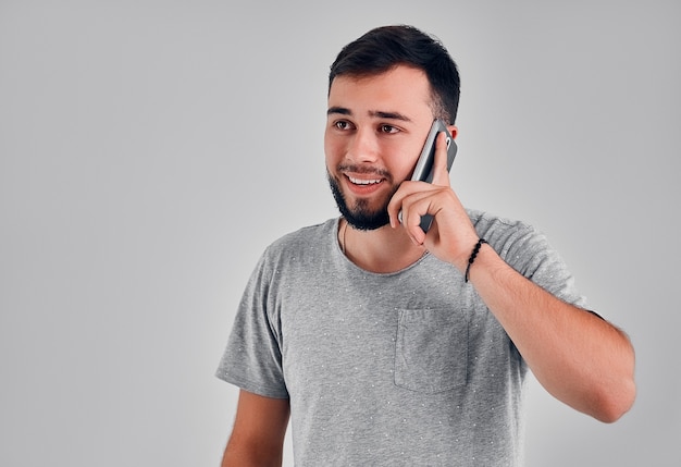 Man on the phone. Cheerful man talking on the mobile phone and smiling while standing isolated on grey