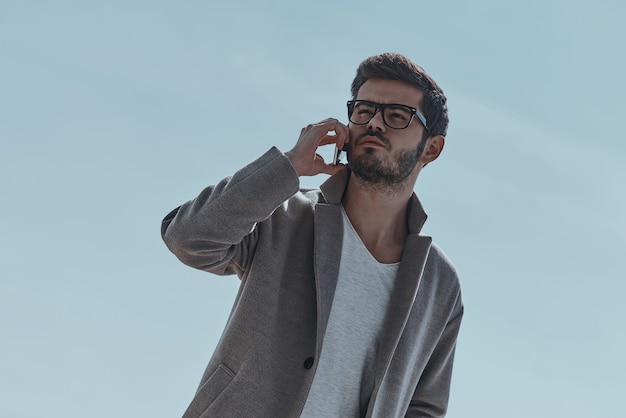 Man on the phone.  Low angle view of serious young modern man talking on the smart phone while standing outdoors