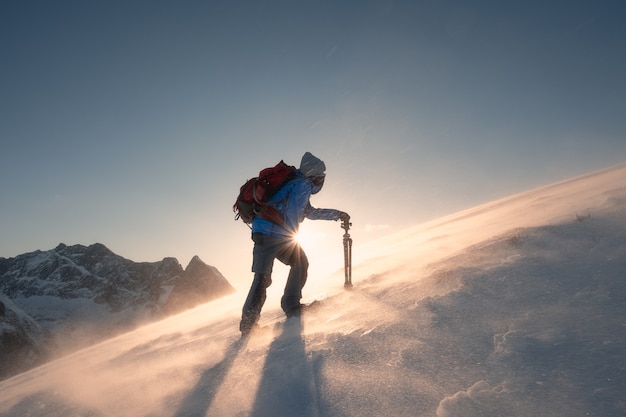 Man photographer with tripod are climbing on slope hill on Ryten mount in blizzard at sunset