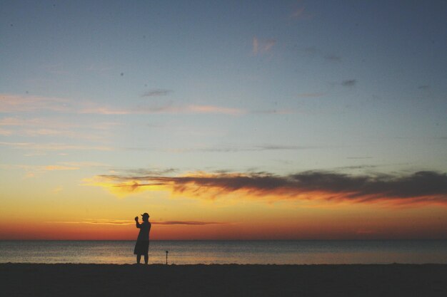 Man photographing at beach against sky during sunset