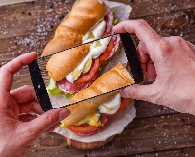 Man photographing sandwich with sausage