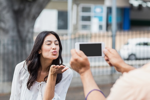 Man photographing woman blowing kiss