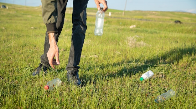 Man picks up a plastic bottles from grass park