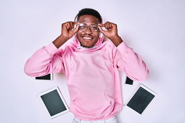 man pink hoodie and glasses lies on white floor listen music holding glasses by phones and a tablet