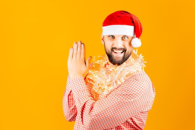 A man in a pink plaid shirt on a yellow background wearing a Santa Claus hat and a garland around his neck