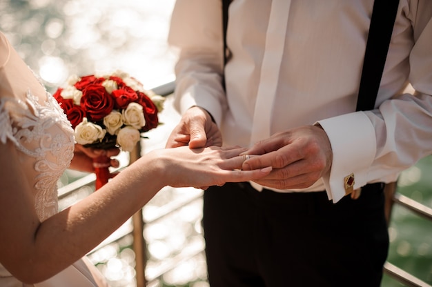 Man placing a ring on the his fiancee finger standing on the pier on the lake. Conception of the wedding