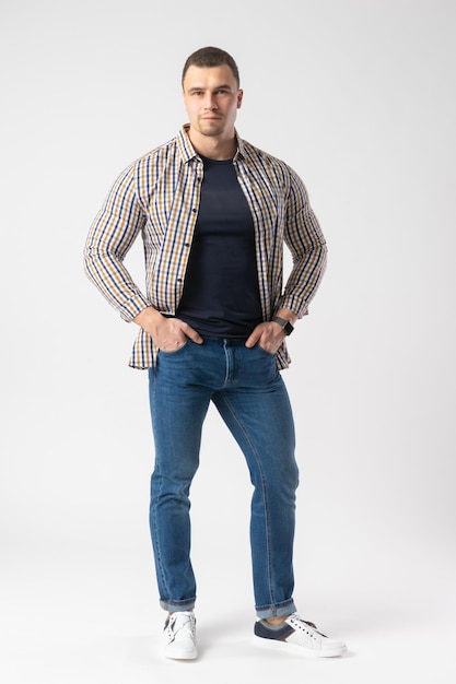 A man in a plaid shirt blue Tshirt and jeans stands with his hands on his hips