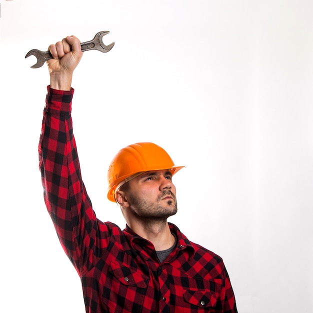 A man in a plaid shirt and construction helmet with a wrench in his hand isolated