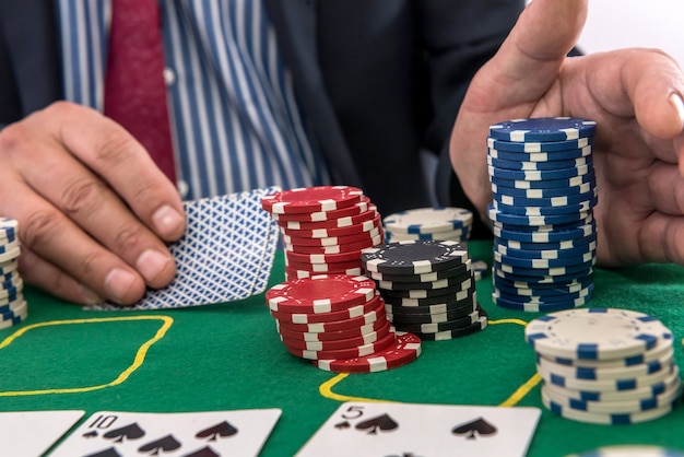 Man play in casino with playing cards and chips at green table. gambling