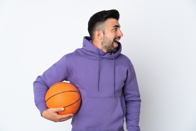 Man playing basketball over isolated white wall laughing in lateral position