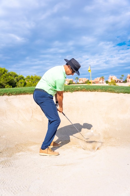 Man playing golf in the bunker hitting the ball with the stick pitching wedge