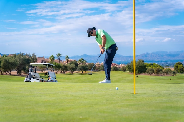 Man playing golf putting the ball into the hole on the green with the putter