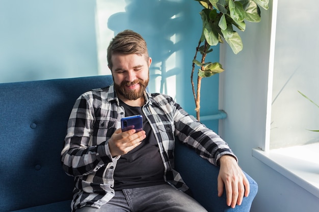 Man playing online games with a smart phone sitting on a couch at home.