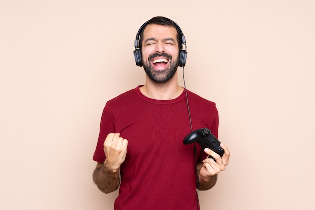 Man playing with a video game controller over isolated wall shouting to the front with mouth wide open