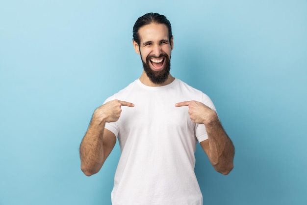 Man pointing fingers on himself and looking at camera with toothy smile extremely satisfied