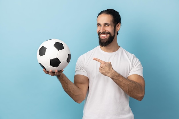 Man pointing at soccer ball in hand and looking at camera with toothy smile