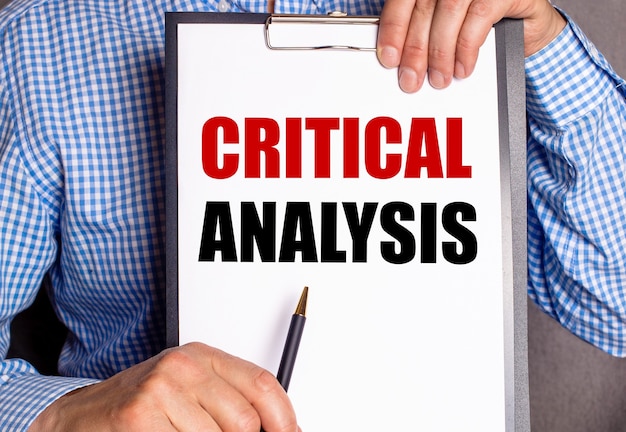 Man points with a pen to the text CRITICAL ANALYSIS on a white sheet.