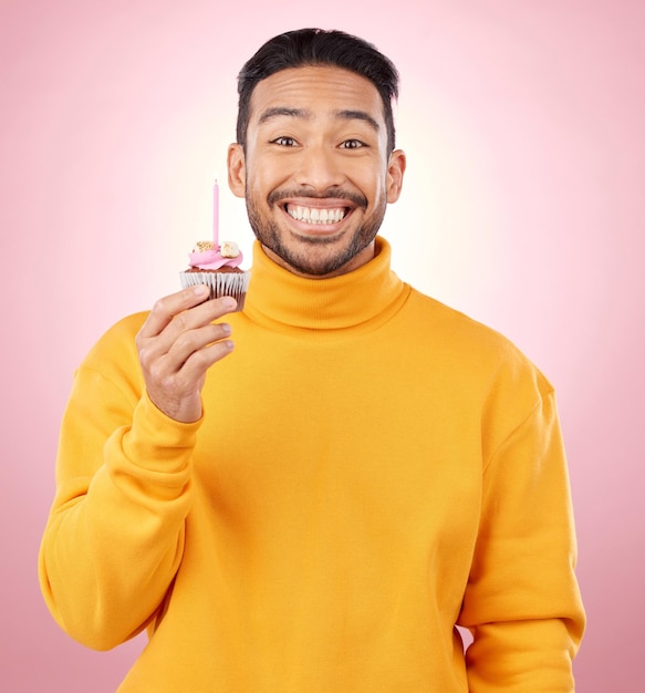 Man portrait and cupcake for birthday celebration and winner success or achievement on pink background Excited happy and young asian person with candle and cake for winning competition in studio