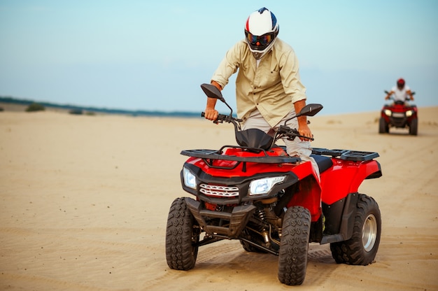 Man poses on atv, downhill riding in desert sands