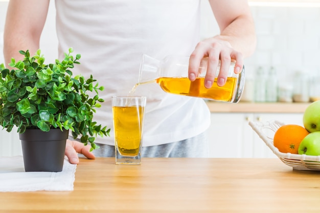 Man pouring apple juice from jug into glass in the kitchen.