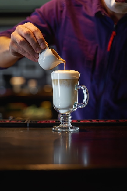 Man pouring frothed milk into espresso making latte coffee. Portrait orientation