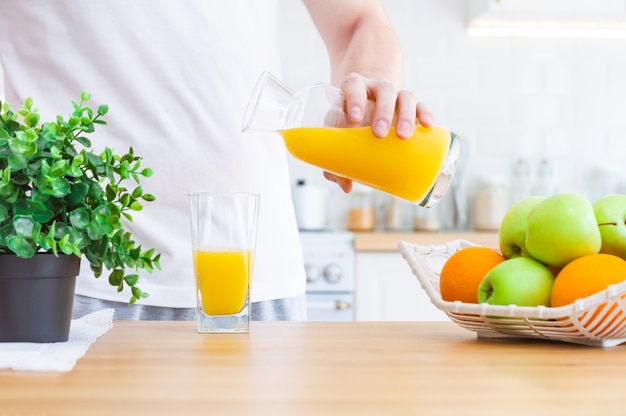 Man pouring orange juice from jug into glass in the kitchen.