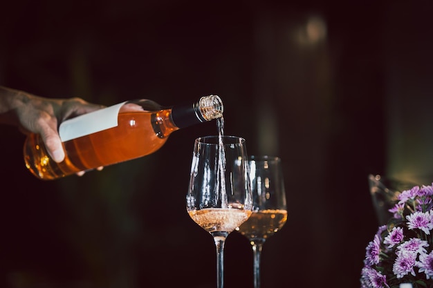 Man pouring rose wine from bottle into glass indoors