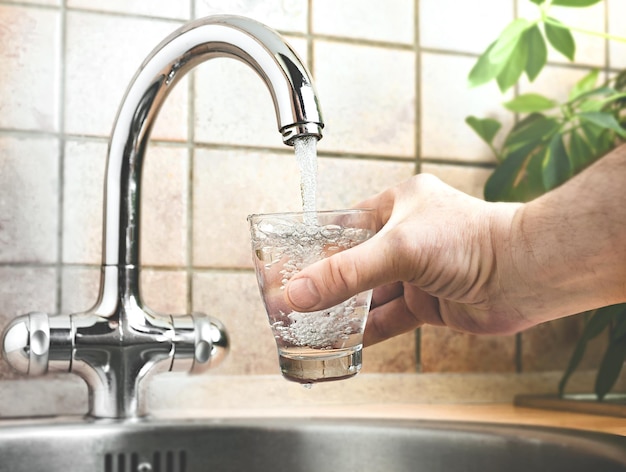 Man pouring water from faucet into glass in kitchen